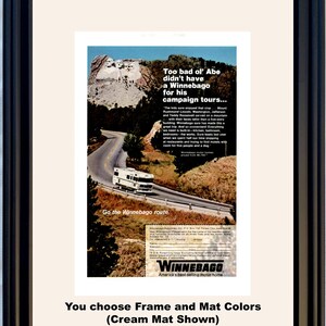 May include: Framed vintage advertisement for Winnebago motorhomes. The ad features a Winnebago RV driving on a scenic road with Mount Rushmore in the background. Text includes "Too bad ol' Abe didn't have a Winnebago for his campaign tours..." and "Go the Winnebago route."