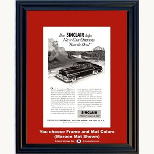 May include: A vintage Sinclair Oil advertisement print featuring a black and white illustration of a car and a devil figure, displayed in a black frame with a maroon mat. The text reads How SINCLAIR helps New Car Owners Beat the Devil.