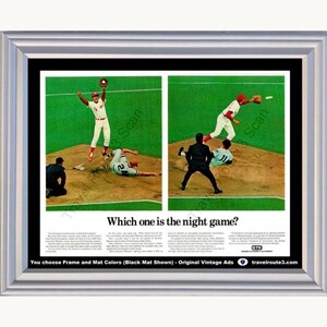 May include: A framed vintage advertisement featuring two baseball game photos side-by-side on a green field with brown dirt. The text reads, Which one is the night game? and includes a GTE logo. The frame is silver with a black mat border.