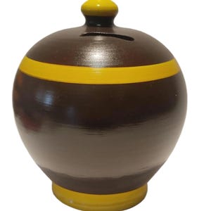 May include: A brown ceramic piggy bank with a yellow stripe and accents. The bank has a slot for coins and a decorative top. The base and top of the bank are yellow, and the body is brown.