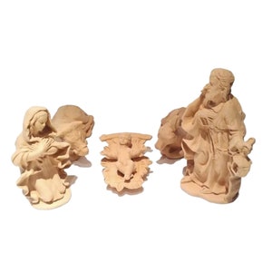 Puede incluir: Un conjunto de figuras de madera tallada, que incluye una figura arrodillada, una figura de pie y una pieza central decorativa. Las figuras, de color marrón claro, parecen formar parte de un belén o una exhibición religiosa.