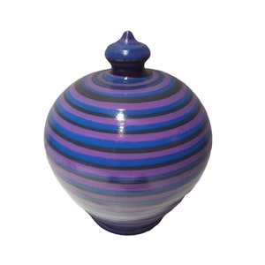 May include: A purple and blue striped ceramic piggy bank with a rounded shape and a small, pointed lid.