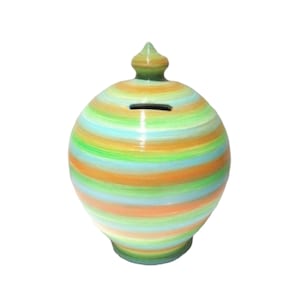 Puede incluir: Una alcancía de cerámica a rayas de colores brillantes. La alcancía redonda tiene una ranura para monedas y una tapa decorativa. Las rayas son en tonos de verde, naranja y azul. Un artículo decorativo para ahorrar.