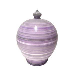 Pode incluir: Um pote decorativo com tampa, corpo bulboso e remate pontiagudo. O pote é pintado com faixas horizontais de várias tonalidades de roxo, cinza e branco. O pote tem um acabamento brilhante e está sobre um fundo branco.
