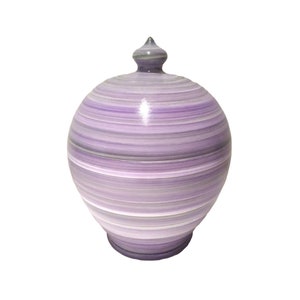 May include: A decorative, lidded jar with a bulbous body and a pointed finial. The jar features horizontal bands of varying shades of purple, gray, and white. The ceramic jar is a decorative item.