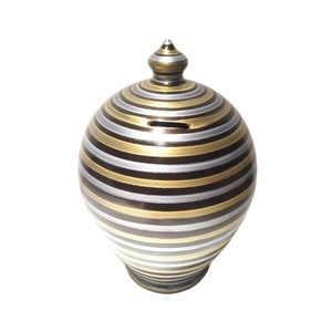 May include: A black, gold, and silver striped ceramic piggy bank with a round shape and a small opening on the top.