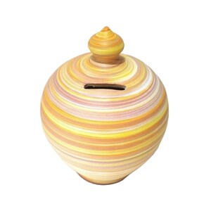 May include: A spherical ceramic piggy bank featuring a horizontal striped pattern in shades of yellow, orange, pink, and white. The object has a pointed lid at the top and a narrow horizontal coin slot located on the upper portion of the body.
