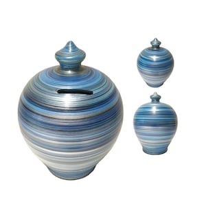 Op de afbeelding: Blauw en zilver gestreepte keramische spaarpot met een puntige deksel. De spaarpot heeft een gleuf voor munten aan de zijkant.