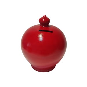 May include: A glossy red ceramic piggy bank with a spherical body and a small, decorative finial on top. The bank has a slot for inserting coins and a rounded base. The overall design is simple and elegant.