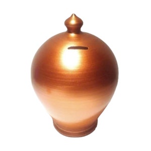 May include: A copper colored ceramic piggy bank with a rounded shape and a small opening on the top for coins.