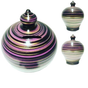 Könnte beinhalten: Zwei Keramik-Sparschweine mit einem Spiralmuster in Schwarz, Pink und Gold. Die Sparschweine haben einen runden Körper und einen kleinen, spitzen Deckel.