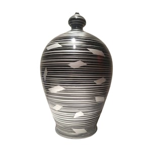 May include: A black and white ceramic piggy bank with a striped pattern and white geometric shapes. The piggy bank has a rounded body and a small lid on top.