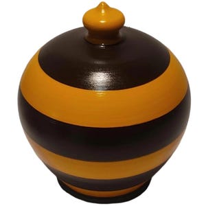 May include: A spherical container with a lid, featuring alternating horizontal stripes of dark brown and bright yellow. The lid has a small, rounded yellow knob at the top. The object has a smooth, polished finish and a circular base.