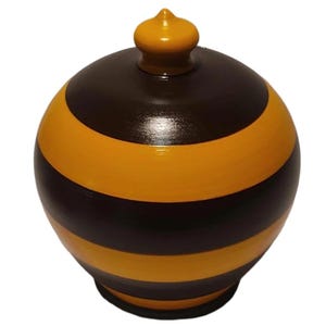 May include: A decorative, hand-painted wooden jar with a lid. The jar is spherical with alternating bands of dark brown and golden yellow. The lid is a matching golden yellow color. The jar has a small, rounded base.