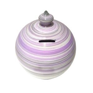 Peut inclure: Une tirelire en céramique rayée de violet et de blanc, de forme arrondie, avec un petit couvercle sur le dessus.