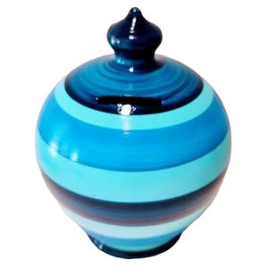 May include: A ceramic piggy bank with a rounded shape, painted with horizontal stripes of varying shades of blue. The bank has a slot for inserting coins and a small, dark blue knob on top.