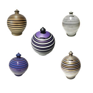 Pode incluir: Um conjunto de cinco cofrinhos de cerâmica decorativos com listras. Os cofrinhos apresentam várias combinações de cores, incluindo preto e dourado, preto e branco, roxo e branco, e azul e roxo. Cada cofrinho tem uma ranhura para moedas e um topo decorativo.