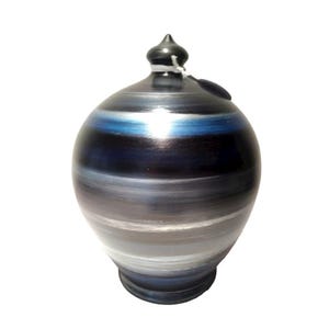 Può includere: Un salvadanaio in ceramica con finitura scura e lucida. La banca presenta fasce orizzontali di colore, tra cui sfumature di blu, grigio e nero. Ha una piccola parte superiore di colore scuro e una fessura per inserire le monete.