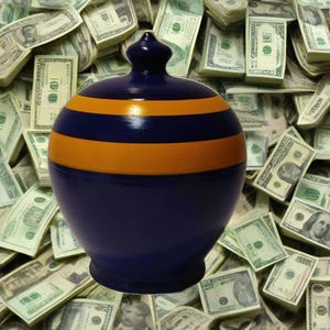 May include: A navy blue ceramic piggy bank with two horizontal orange stripes. The piggy bank has a rounded shape and a small, decorative top. The background is a pile of US dollar bills.