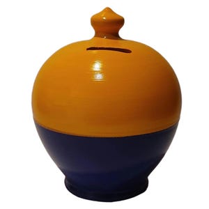 May include: A two-tone ceramic piggy bank. The top half is painted a bright yellow-orange, and the bottom half is a deep blue. It has a slot for inserting coins and a small, pointed finial on top.