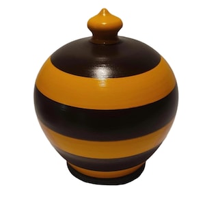 May include: A spherical jar with a glossy finish featuring alternating horizontal stripes of dark brown and bright yellow. The container has a matching yellow lid with a small, rounded finial at the top and a dark brown base.