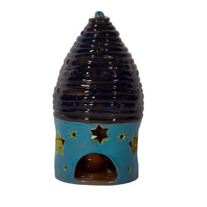 Puede incluir: Un portavelas de cerámica con diseño de colmena. La sección superior es azul oscuro con pequeños agujeros, y la base es azul claro con recortes en forma de estrella. Es un artículo decorativo.