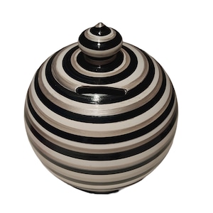 Peut inclure: Une tirelire sphérique présentant un motif répétitif de rayures horizontales noires, blanches et grises. L'objet possède un couvercle amovible avec un petit bouton pointu au sommet et une fente horizontale pour pièces sur la partie supérieure.