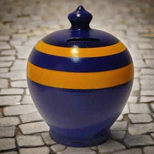 May include: A blue ceramic piggy bank with two horizontal yellow stripes. The bank has a rounded shape with a small slot on top for inserting coins. It features a small, pointed finial on the lid.