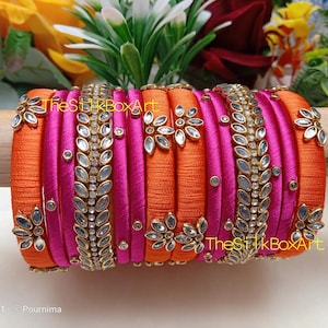 Può includere: Un set di 10 braccialetti in filo di seta rosa e arancio con decorazioni. I braccialetti sono adornati con strass trasparenti e dettagli dorati.