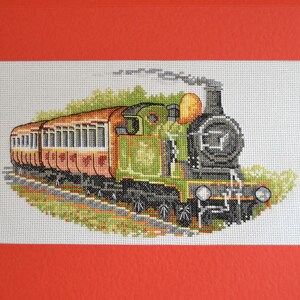 May include: A cross-stitch pattern of a green and black steam train with red and brown passenger cars. The train is surrounded by green foliage.