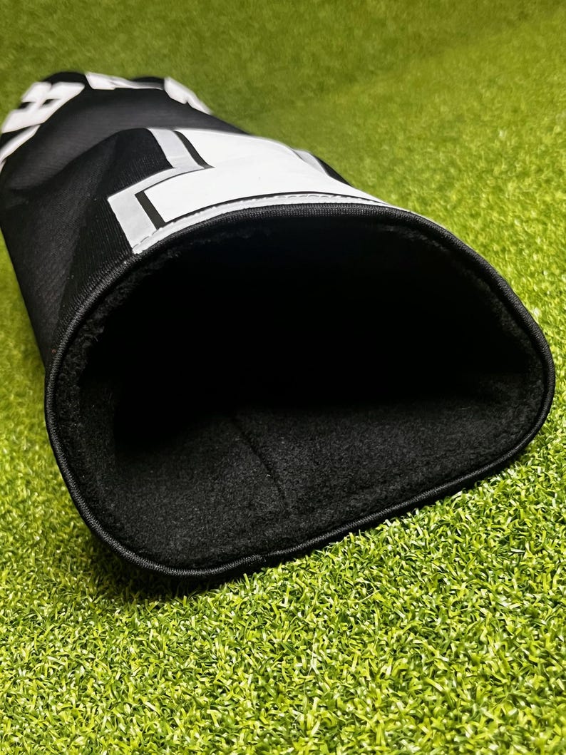 Peut inclure: Une housse de club de golf noire avec un motif graphique blanc sur l'ext&eacute;rieur et une doublure en polaire noire douce &agrave; l'int&eacute;rieur. La surface ext&eacute;rieure pr&eacute;sente des lettres blanches partielles et des formes g&eacute;om&eacute;triques.