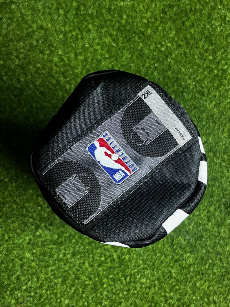 Peut inclure: Un maillot de sport noir dot&eacute; d'un &eacute;cusson rectangulaire gris avec le logo NBA Authentics, un graphique de terrain de basket et l'&eacute;tiquette de taille 2XL. Le v&ecirc;tement est fabriqu&eacute; dans un tissu en maille textur&eacute; et respirant avec des coutures visibles.