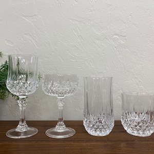 May include: Four clear glass drinking glasses with a diamond pattern. The glasses are arranged in a row from left to right, with the largest glass on the left and the smallest glass on the right.