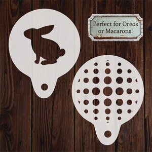 Könnte beinhalten: Zwei weiße Kunststoff-Schablonen, eine mit einer Hasen-Silhouette und die andere mit einem Kreis-Muster. Der Text "Perfekt für Oreos oder Macarons!" befindet sich auf einem Metallschild.
