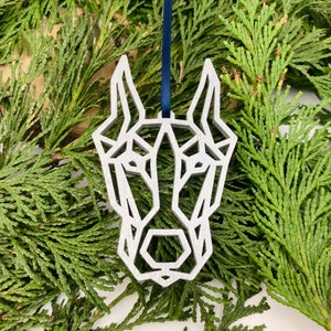 May include: A silver geometric dog ornament with a blue ribbon for hanging on a Christmas tree.