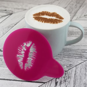 May include: A pink plastic stencil shaped like a pair of lips. The stencil is used to create a design in coffee foam.
