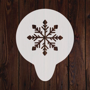 Op de afbeelding: Witte plastic sneeuwvlokstencil voor knutselen en decoreren. De stencil heeft de vorm van een sneeuwvlok met zes punten en een gedetailleerd ontwerp.