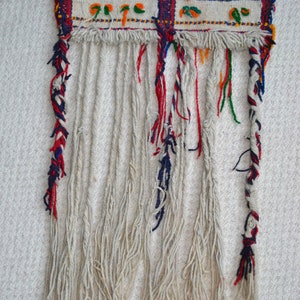 May include: A woven tapestry with a red, white, and blue fringe. The tapestry has a geometric pattern with red, white, blue, green, and yellow colors.