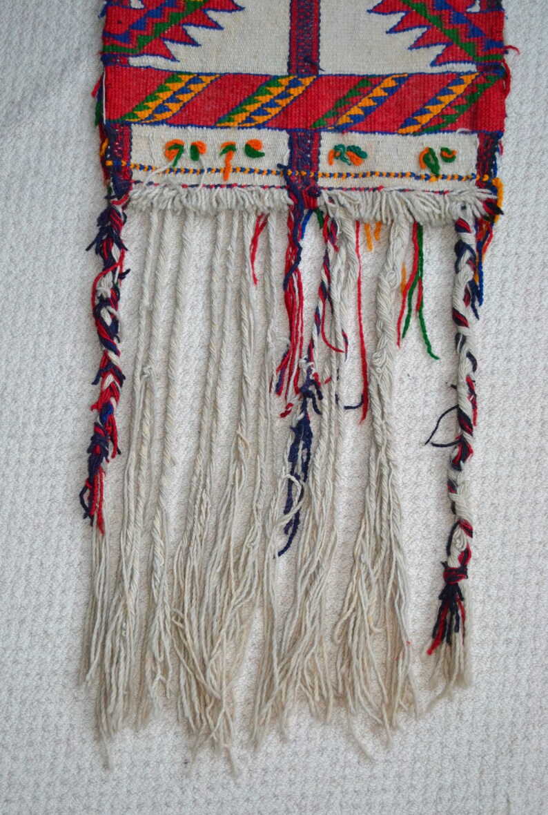 May include: A woven tapestry with a red, white, and blue fringe. The tapestry has a geometric pattern with red, white, blue, green, and yellow colors.