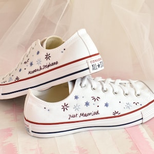 May include: A pair of white Converse sneakers with blue and red embroidery. One shoe says "Just Married" and the other says "Manon & Stephane".