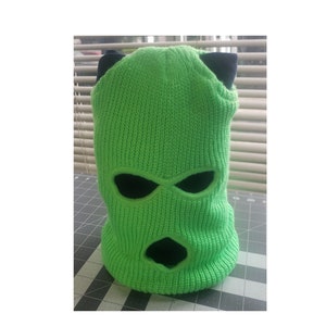 May include: A bright green ski mask with black eye and mouth holes. The mask has two small black ear flaps on top.