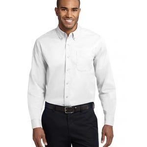 K&ouml;nnte beinhalten: Ein wei&szlig;es Langarmhemd mit klassischem Button-Down-Kragen, einer Brusttasche auf der linken Seite und einer durchgehenden Knopfleiste. Das Hemd wird mit einer dunkelblauen Hose und einem schwarzen G&uuml;rtel kombiniert.