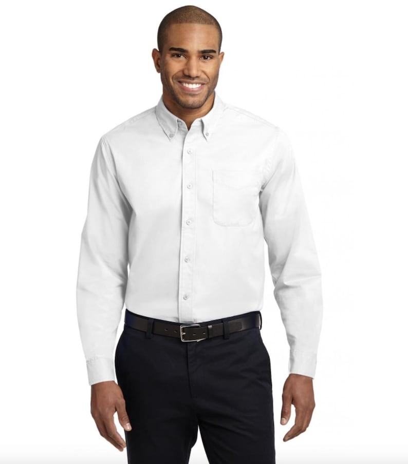 K&ouml;nnte beinhalten: Ein wei&szlig;es Langarmhemd mit klassischem Button-Down-Kragen, einer Brusttasche auf der linken Seite und einer durchgehenden Knopfleiste. Das Hemd wird mit einer dunkelblauen Hose und einem schwarzen G&uuml;rtel kombiniert.