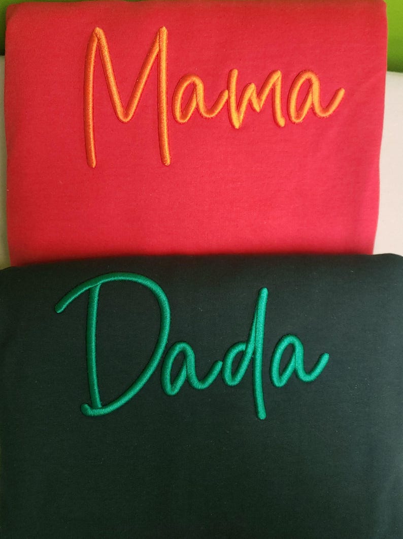 May include: Two sweatshirts, one red with the word "Mama" embroidered in orange, and one black with the word "Dada" embroidered in green.