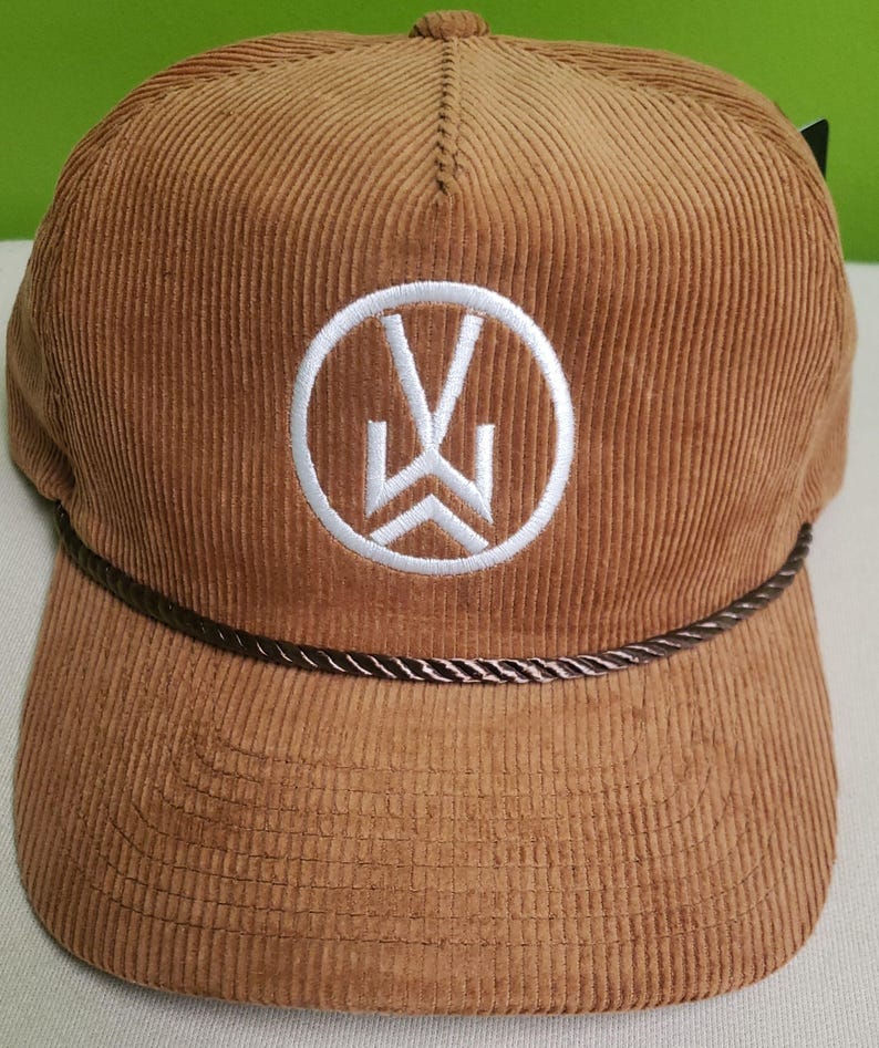 Puede incluir: Una gorra de b&eacute;isbol de pana marr&oacute;n con un logotipo bordado en blanco de un c&iacute;rculo con una "W" estilizada en su interior. La gorra tiene un ribete de cuerda marr&oacute;n alrededor de la visera.