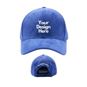 Puede incluir: Una gorra de béisbol de gamuza azul con bordado blanco que dice "Your Design Here" en la parte delantera y "Arch Embroidery" en la parte posterior.