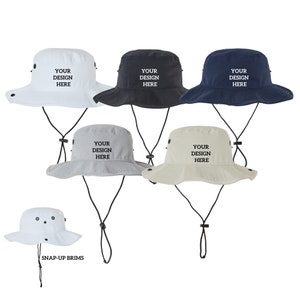 May include: Five different colored bucket hats with adjustable straps. The hats are white, black, navy blue, light gray, and beige. Each hat has the text "YOUR DESIGN HERE" printed on the front.