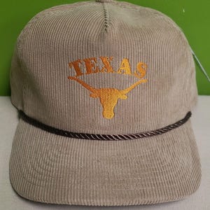 Puede incluir: Una gorra de b&eacute;isbol de pana beige con ribete de cuerda marr&oacute;n. La gorra tiene un logotipo bordado de Texas Longhorn naranja con la palabra "TEXAS" encima.