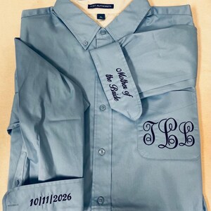 K&ouml;nnte beinhalten: Ein hellblaues Hemd mit Knopfleiste, Port Authority-Etikett und XL-Gr&ouml;&szlig;enangabe. Das Hemd ist dunkelblau bestickt: auf der Brusttasche mit dem Monogramm JLL, auf einer Manschette mit Mother of the Bride und auf der anderen mit 10/11/2026.