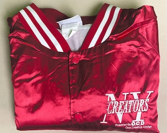 May include: A shiny red satin varsity jacket featuring a white striped collar and snap button closure. The front displays white embroidered text that reads CREATORS, with smaller text below stating Powered By O.C.D One Creative Design.